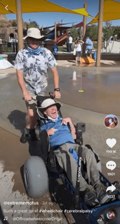 A man pushing his friend in an adapted wheelchair meant for outdoor activity.