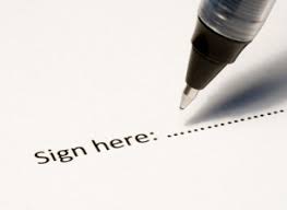 Image description: A white sheet of paper with the words "Sign here" followed by a dotted line. A tip of a pen hovers over the line.