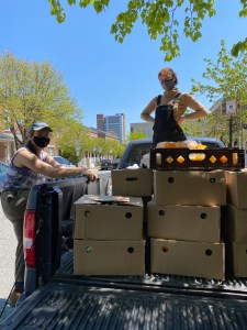 Two of my comrades posing next to and on a blue pick up truck full of brown boxes full of food