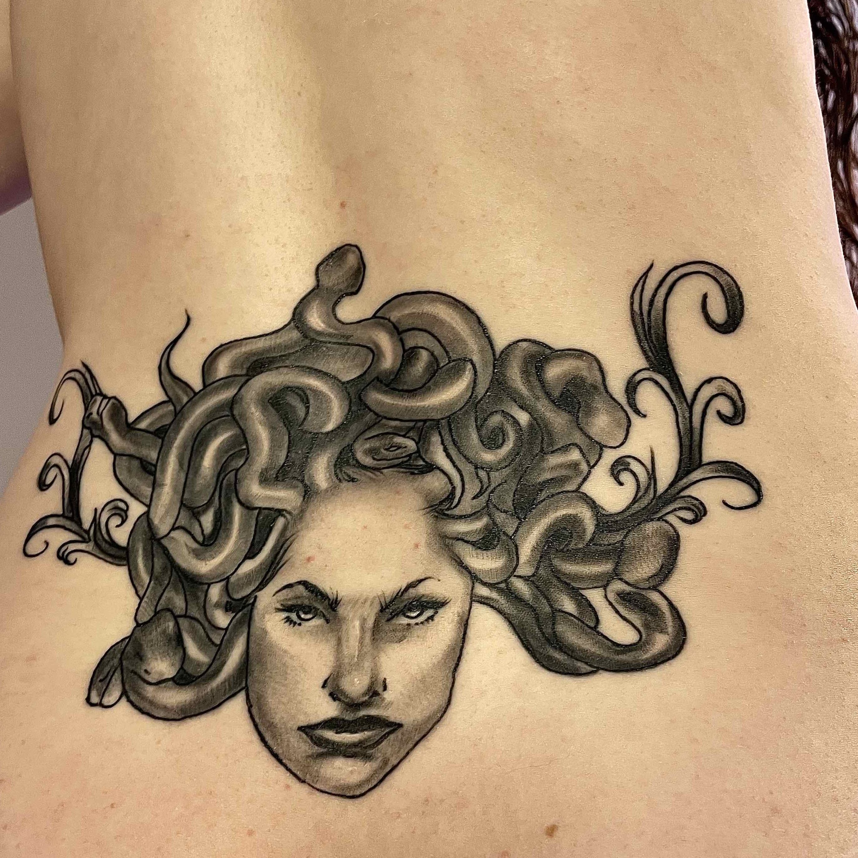 Lower back tattoo of Medusa's head in black and white. 