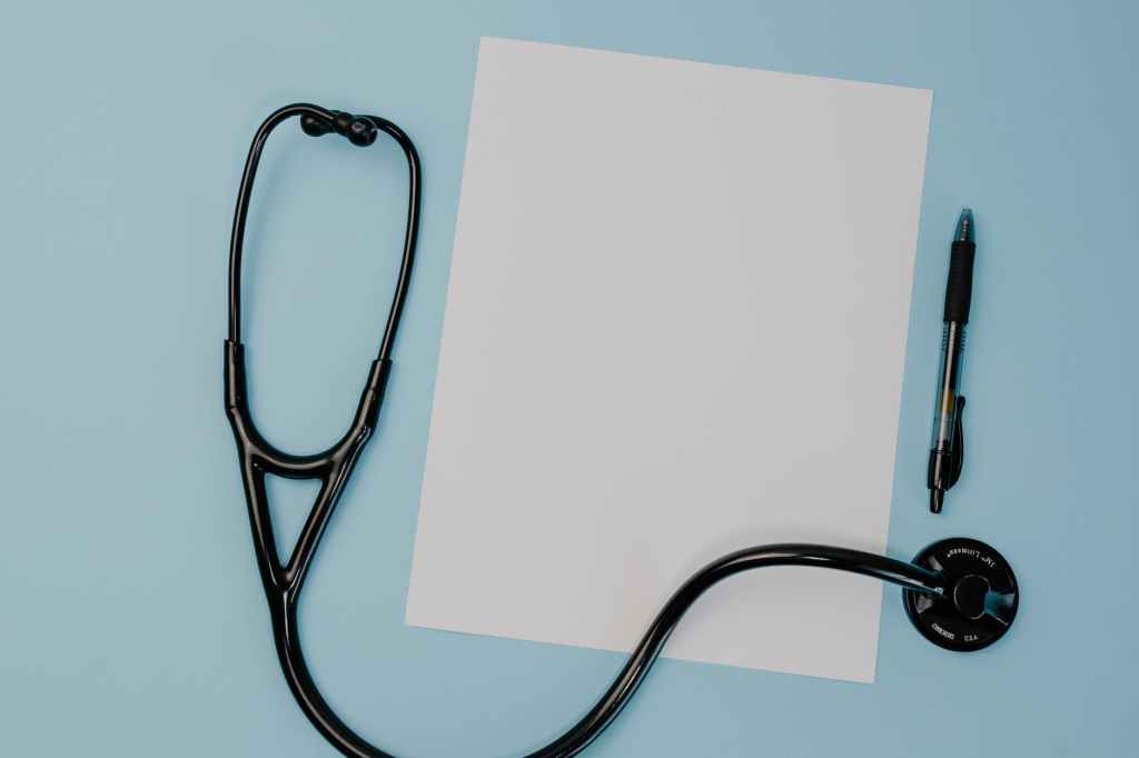 A photo of a blank piece of white paper, a black stethoscope, and a black pen on a light blue background