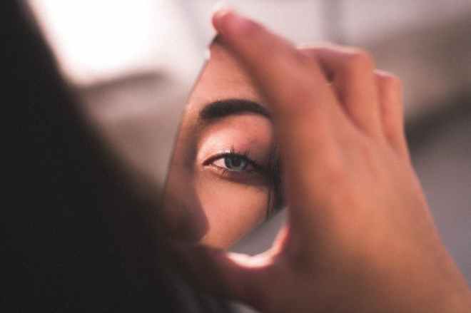 woman looking at her sad eye in a broken mirror