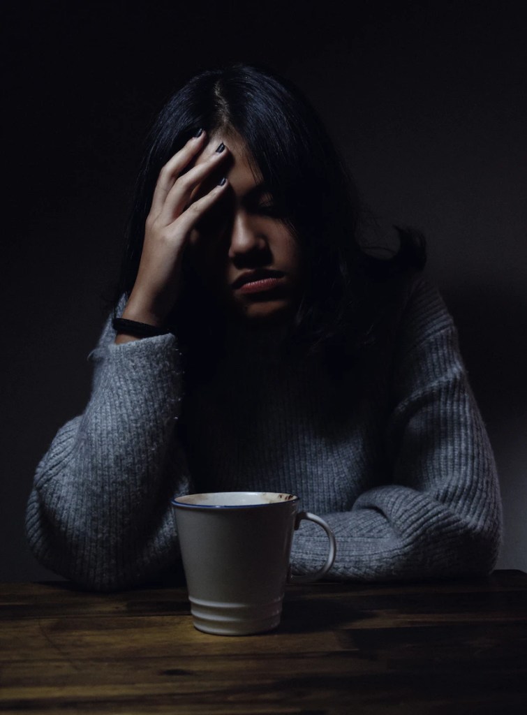 Person sitting at a table in the dark with a hand on their forehead looking tired.
