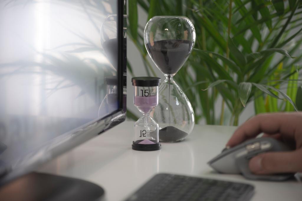 Two hourglasses sit on a desk as a person uses their computer.