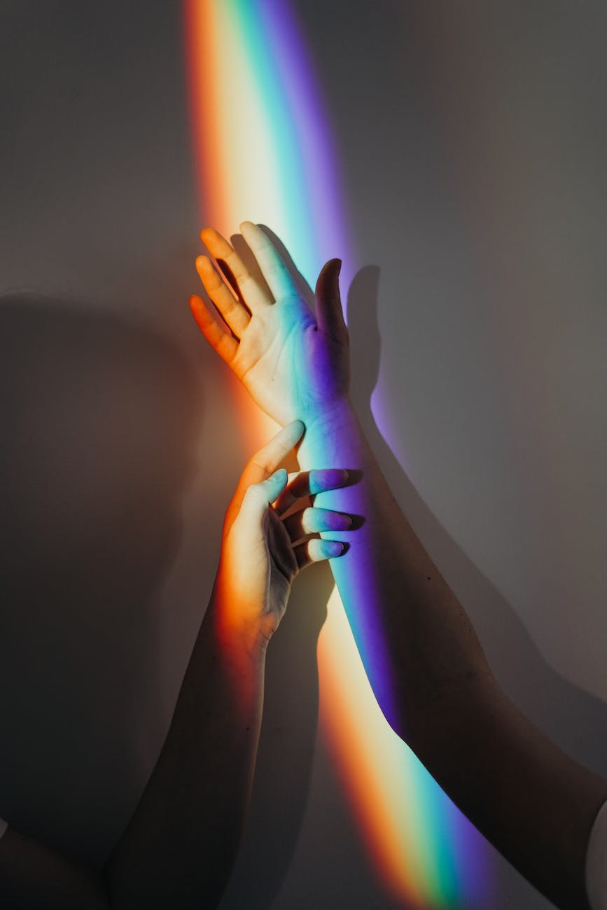 Image showing two arms reaching out in a dark room, with nothing but a rainbow cast on them.