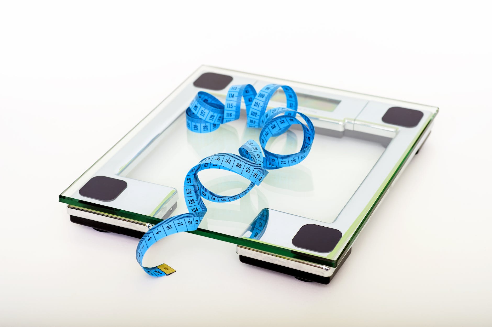 An image of a glass electronic scale, one you can step on. There is a blue measuring tape lying on top of it.