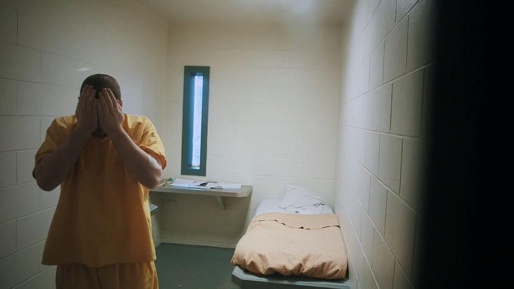 An inmate standing in the middle of the cell with both hands covering their face